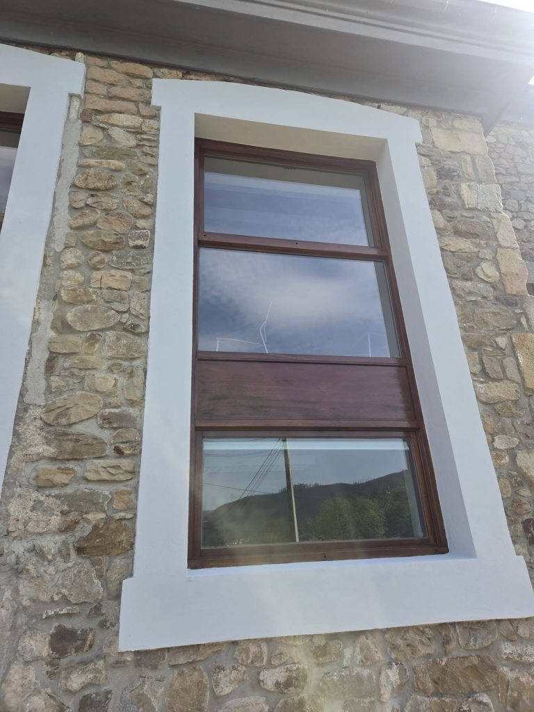 Fachada de piedra rehabilitada con recercado blanco y carpintería de madera restaurada