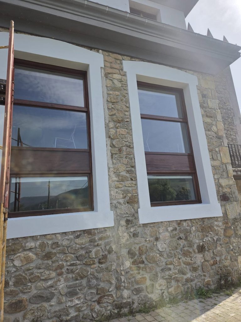 Fachada de piedra rehabilitada con ventanas de madera y recercados blancos