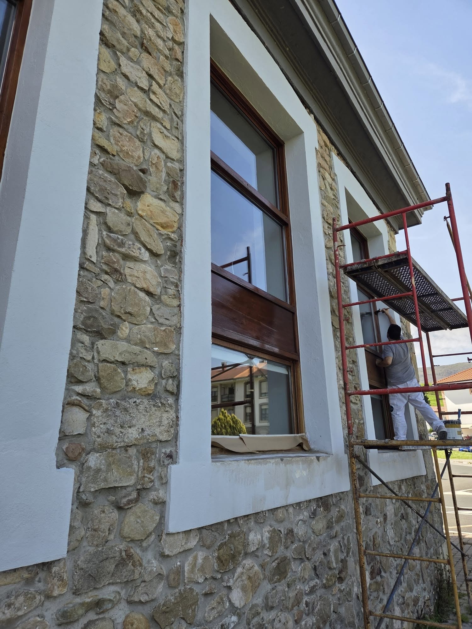 Albañil rehabilitando una fachada de mampostería de piedra desde andamio en Cantabria